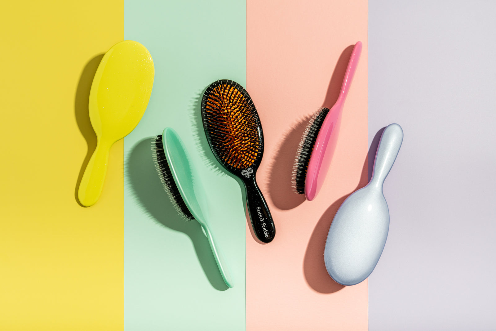 Super sized brushes in Lemon yellow, Ice Blue, Lavender, Bright Pink and Black on a stripy coloured background.